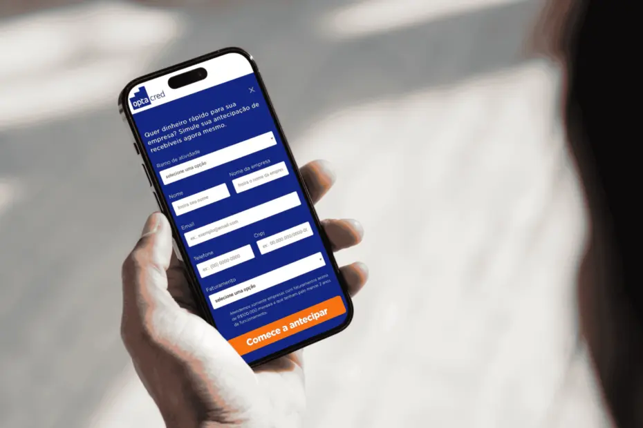 Imagem de um mockup. Uma mão segurando um celular. No celular, um formulário da Optacred para antecipação de vendas